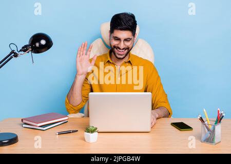 Portrait of positive successful person sit chair arm palm wave hi speak communicate video call netbook isolated on blue color background Stock Photo
