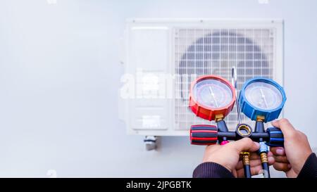 Air repair mechanic using measuring equipment for filling industrial factory air conditioners and checking maintenance outdoor air compressor unit. Stock Photo
