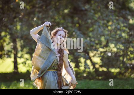 Portrait of a beautiful mature woman dressed in a nymph-style dress inspired by early 20th century artists.Happy woman in the garden on a sunny day Stock Photo