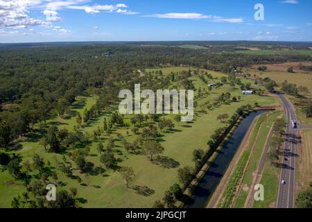 Aerial view of a lush green landscape with a road cutting through, surrounded by trees under a blue sky Stock Photo