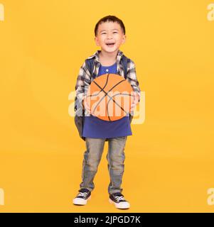 Happy smiling  boy  holding  basketball isolated on yellow background Stock Photo