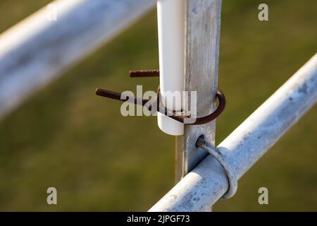 rusty clamp holding a section of plastic pipe to the back section of some bleachers Stock Photo