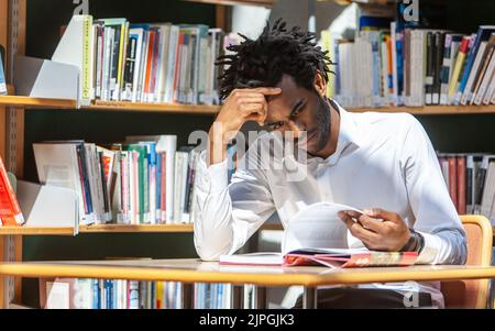 Teenage Students, reading library. A young adult man reading through reference material in a library. From a series of related images. Stock Photo