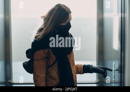 Woman in face medical mask with hand in glove forefinger pressing the button elevator during coronavirus pandemic covid-19 quarantine concept. Stock Photo