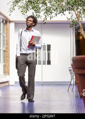 Teenage Students, teacher. A young college tutor walking through the school halls to his next class. From a series of related images. Stock Photo