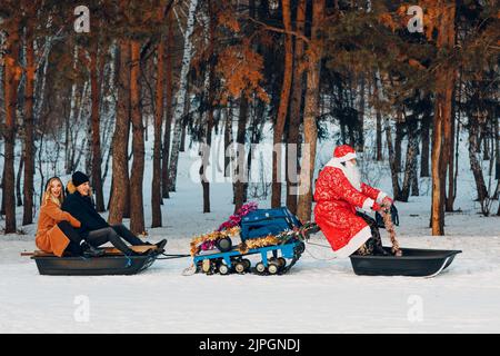 Santa claus riding on snowmobile young couple in love in the winter forest. New year party. Stock Photo