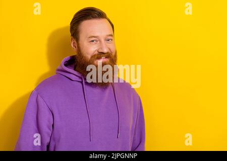 Portrait of positive young guy in comfy violet hoodie have long ginger beard isolated on yellow color background Stock Photo