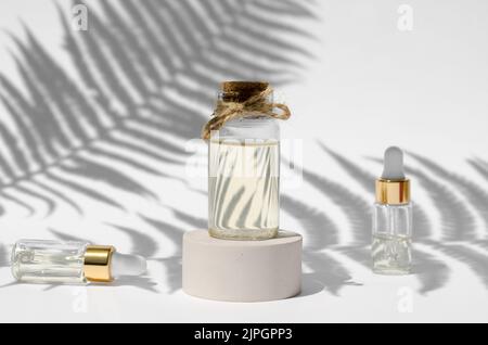 Bottles of natural essential oils on a white background with harsh shadows from fern leaves. Natural cosmetic. Skin care concept Stock Photo