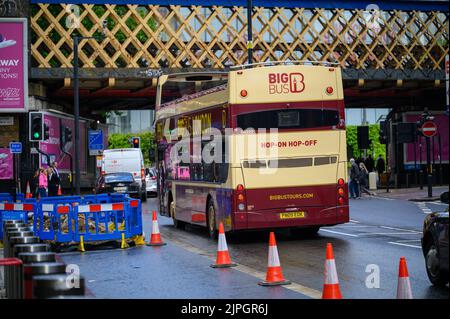 LONDON - May 20, 2022: Open top London Double Decker Tour Bus in road works beneath rail bridge outside Waterloo Station Stock Photo