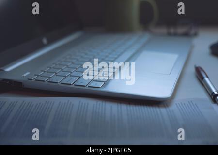 Laptop on a desk with work papers, pen, cup, glasses and mouse in soft light for work Stock Photo