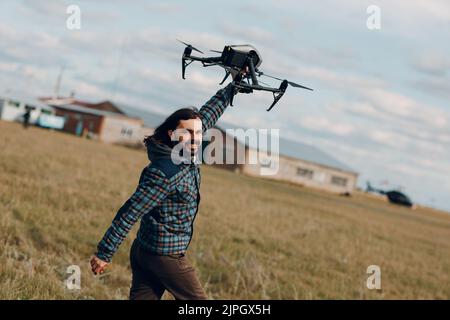 Man pilot holding quadcopter drone in handand running at outdoor field Stock Photo