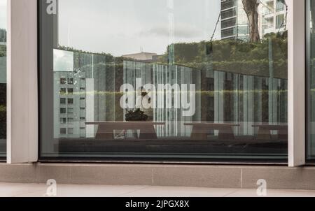 Bangkok,Thailand - Aug 13, 2022 : Looking through glass wall saw a young asia woman sitting on Modern wood bench in Lobby room. She is view smart phon Stock Photo