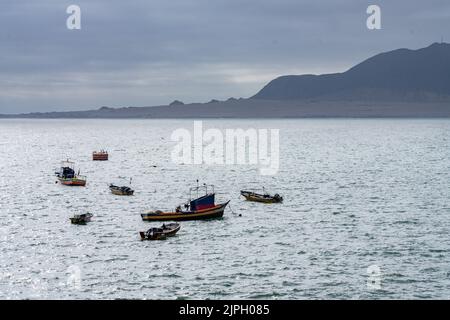 Small open fishing boats moored in the harbor in the port of Chanaral in northern Chile with the Chilean Coastal Range behind. Stock Photo