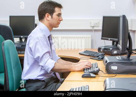 Computer Work. A mature adult male working on a computer in an open office environment. From a series of images with the same theme. Stock Photo