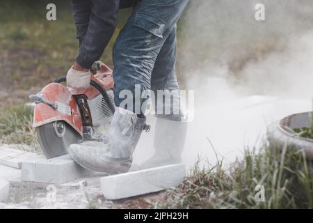 Worker mason cuts the sidewalk tile with circular saw while repairing sidewalk in city street. Stock Photo