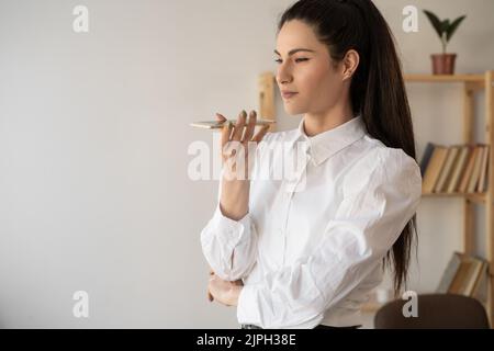 Serious businesswoman or office worker working using smart phone voice recognition to send message, record audio voice message on smartphone Stock Photo