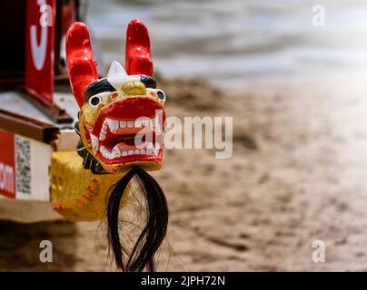 Black, red and gold painted wooden dragon head with chin beard on the bow of a dragon boat, selective focus