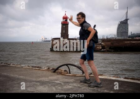 Bremerhaven, Germany. 18th Aug, 2022. A woman simulates the shoring of the tower, in the style of the Leaning Tower of Pisa, with the sagging Mole Tower. The entrance to the Geeste is closed. The ferry service of the Weser ferry also had to be temporarily suspended. Credit: Sina Schuldt/dpa/Alamy Live News Stock Photo