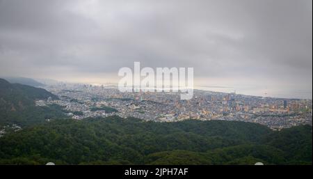 Low fog over sprawling city between forested mountains and bay at dawn Stock Photo