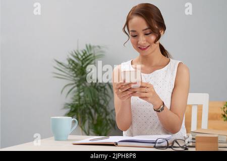 Beautiful young Vietnamese business executive using application in her smartphone Stock Photo
