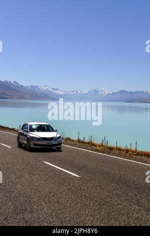 A car on State Highway 8 runs along Lake Tekapo's shore in Mackenzie Country, South Island in New Zealand.  In the distance are the snow-ca Stock Photo