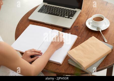 Female student writing notes in her textbook when sitting in cafe Stock Photo
