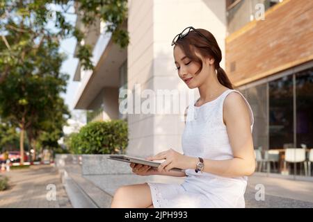 Smiling Vietnamese young woman using application on tablet computer Stock Photo