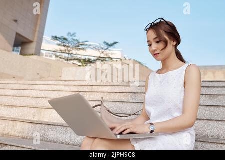 Beautiful young Asian woman busy with work on her laptop Stock Photo