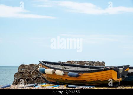 lobster pots traps and orange boat on the beach at Selsey West Sussex England with the sea and blue sky in the background Stock Photo