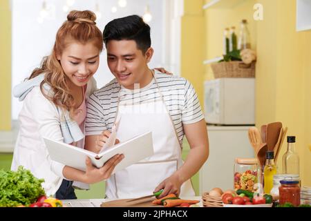 Young Vietnamese couple searching for good recipe in a cookbook Stock Photo