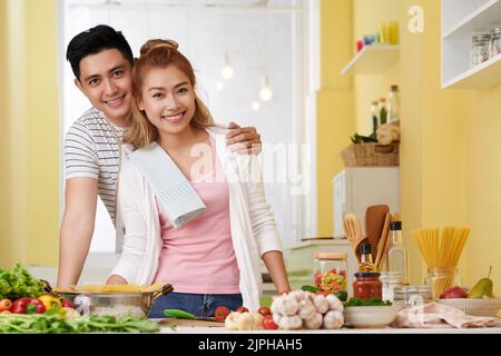 Portrait of happy hugging young Asian couple standing in kitchen Stock Photo
