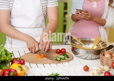 Cropped image of young man making salad when his is girlfriend using mobile app Stock Photo