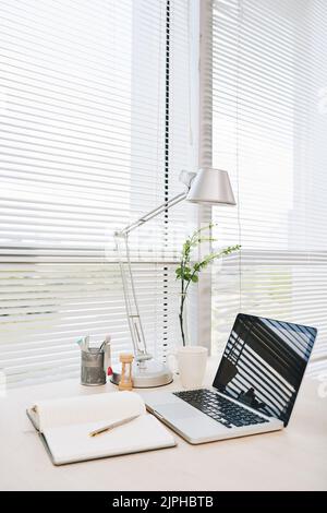 Laptop and opened notepad on tablet near office window Stock Photo