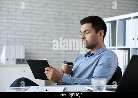 Serious business executive drinking coffee and reading information on talet computer Stock Photo