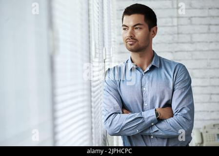 Pensive young businessman looking at the street through office window Stock Photo