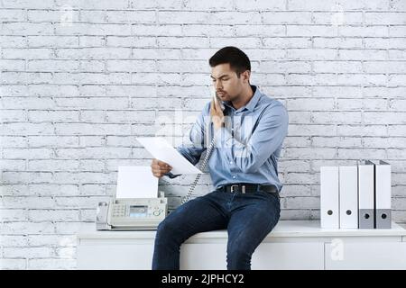 Serious young businessman reading document and talking on the phone Stock Photo