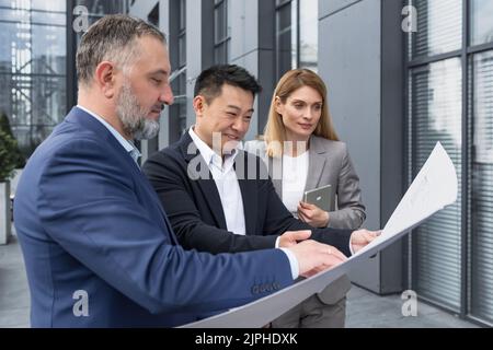 Diverse group of business people outside office building, discussing and talking man and woman discussing new construction plan, team of business people holding and looking at construction project Stock Photo