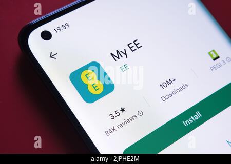 My EE app seen in Google Play Store on the smartphone screen placed on red background. Close up photo with selective focus. Stafford, United Kingdom, Stock Photo