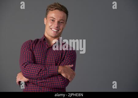 Studio portrait of handsome smiling young man standing with his arms crossed Stock Photo