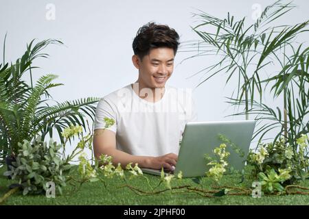 Happy freelancer working on laptop in green environment Stock Photo