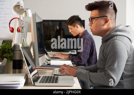 Group of talented young programmers sitting at spacious open plan office and working on brand-new computer application, profile view Stock Photo
