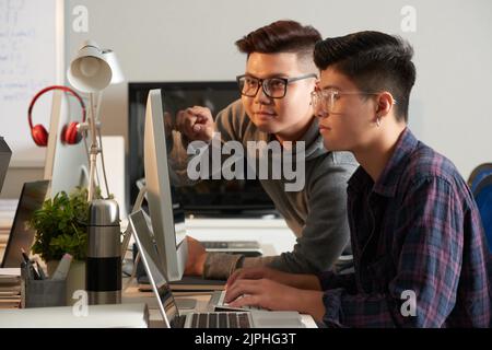 Group of talented young managers in casualwear gathered together in front of modern computer and working on start-up project, interior of open plan office on background Stock Photo