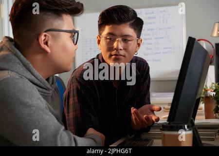 Handsome young programmers wearing eyeglasses having productive discussion of joint project while sitting at spacious open plan office Stock Photo