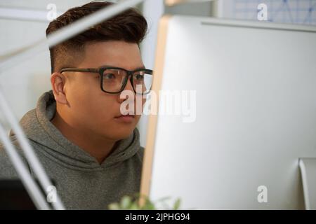 Head and shoulders portrait of confident young student wearing hoodie and eyeglasses sitting in front of modern computer while having ICT class Stock Photo