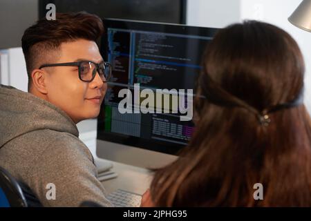 Group of talented programmers sitting in front of modern computer and writing programming code while working together at open plan office Stock Photo