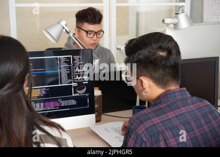 Back view of male and female programmers working together on ambitious project while sitting at spacious open plan office Stock Photo