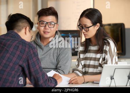 Group of talented young white collar workers gathered together at open plan office and brainstorming on promising project, handsome Asian man looking at camera Stock Photo