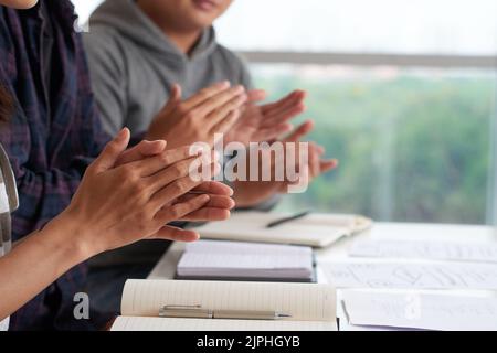 Group of managers sitting at desk and clapping their hands after completion of business conference, close-up shot Stock Photo