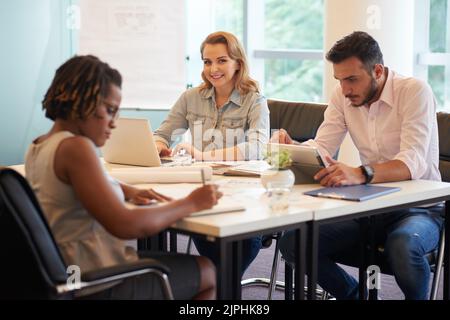 Male and female colleagues gathered together at spacious boardroom and brainstorming on their joint project, pretty young manager with long blonde hair looking at camera with charming smile Stock Photo