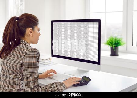 Female accountant calculates company's financial accounts using calculator and computer program. Stock Photo